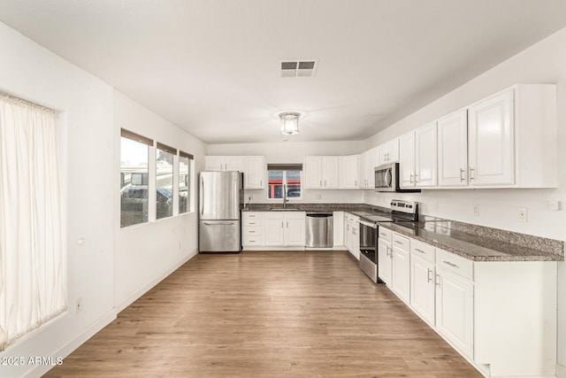 kitchen featuring sink, white cabinetry, light wood-type flooring, appliances with stainless steel finishes, and dark stone counters