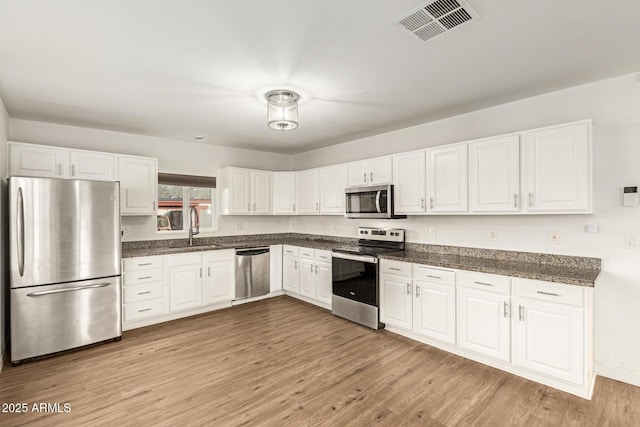 kitchen with stainless steel appliances, sink, white cabinets, and light hardwood / wood-style flooring