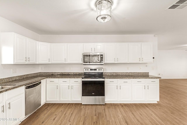 kitchen with sink, dark stone countertops, white cabinets, stainless steel appliances, and light hardwood / wood-style flooring