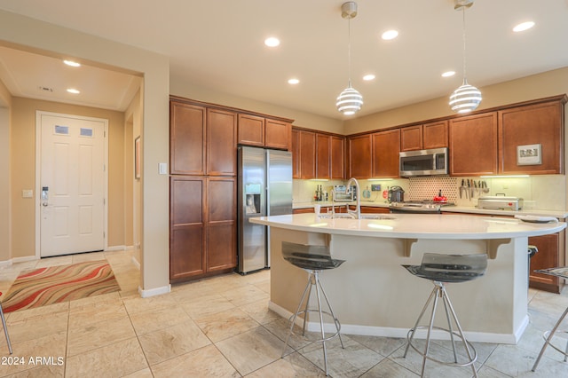 kitchen featuring appliances with stainless steel finishes, hanging light fixtures, tasteful backsplash, and an island with sink