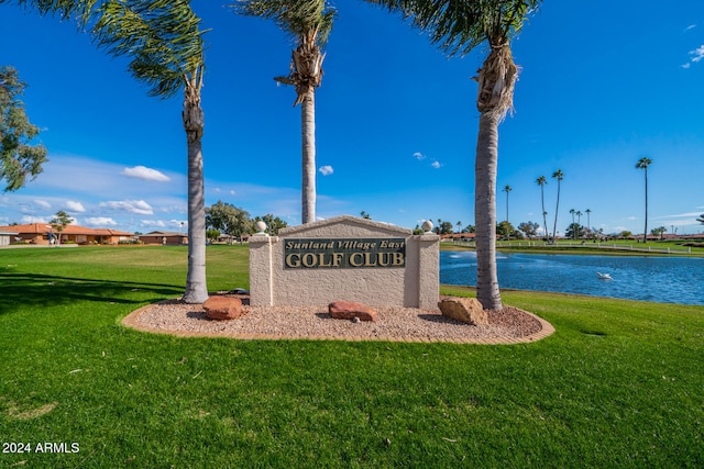 community / neighborhood sign featuring a lawn and a water view