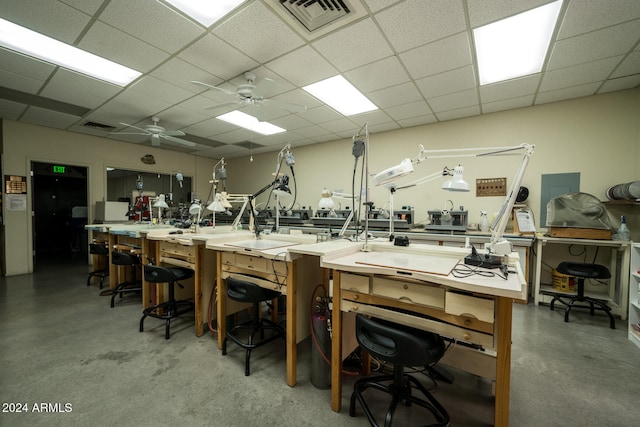 interior space featuring a paneled ceiling, ceiling fan, a workshop area, and concrete flooring