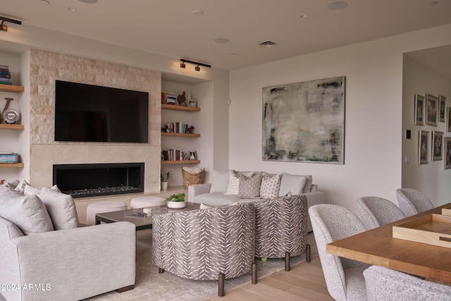 living room with light wood-type flooring, a fireplace, and built in features