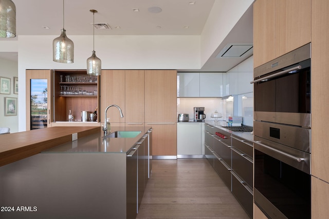 kitchen featuring hanging light fixtures, multiple ovens, white cabinets, sink, and dark wood-type flooring