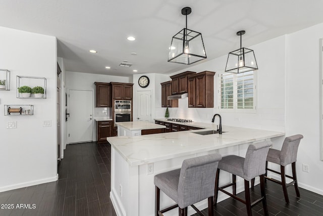 kitchen featuring sink, pendant lighting, stainless steel appliances, kitchen peninsula, and a breakfast bar area