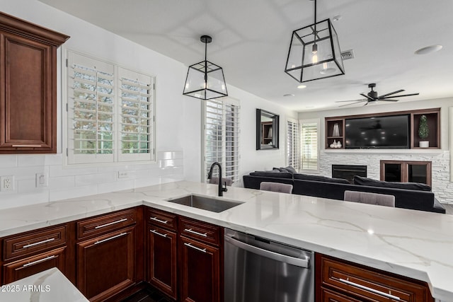 kitchen with decorative light fixtures, a stone fireplace, sink, stainless steel dishwasher, and light stone counters