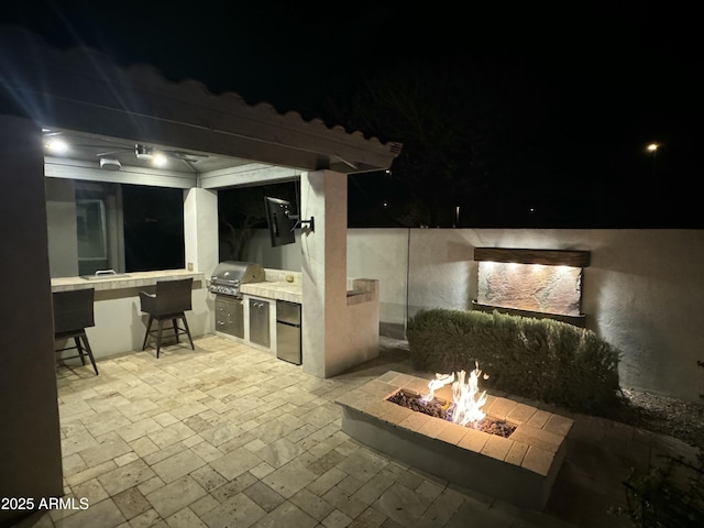 patio at night featuring area for grilling, exterior bar, a grill, and an outdoor fire pit