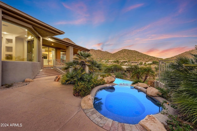 pool at dusk featuring an outdoor pool, a mountain view, fence, and a patio area