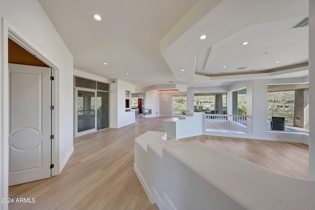 hallway featuring a tray ceiling, light hardwood / wood-style floors, and a healthy amount of sunlight