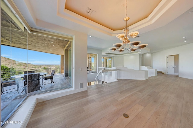 interior space with a mountain view, a raised ceiling, a chandelier, and light wood-type flooring