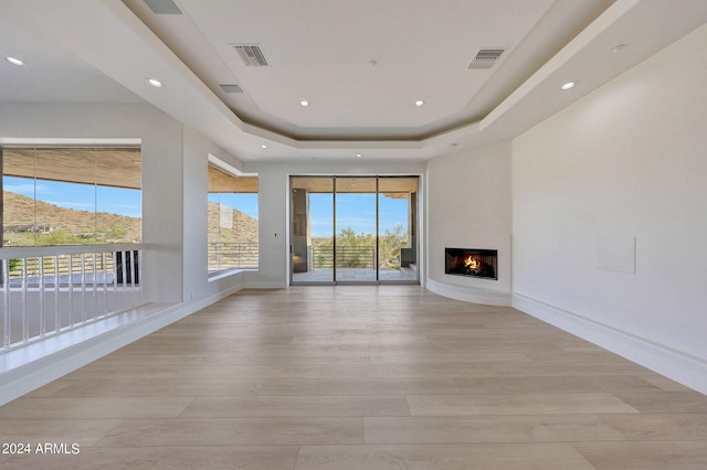 unfurnished living room with a tray ceiling, a mountain view, and light hardwood / wood-style flooring