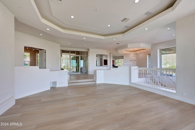 spare room with a raised ceiling, a wealth of natural light, and light hardwood / wood-style flooring