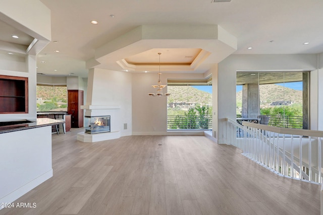 unfurnished living room featuring a tray ceiling, light hardwood / wood-style floors, a healthy amount of sunlight, and a multi sided fireplace