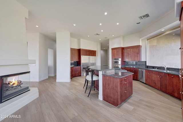 kitchen with a multi sided fireplace, a kitchen island, light hardwood / wood-style floors, and appliances with stainless steel finishes