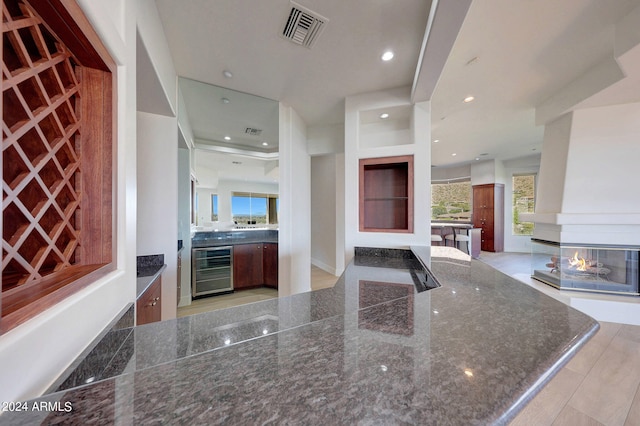 kitchen with a multi sided fireplace, beverage cooler, and dark stone countertops