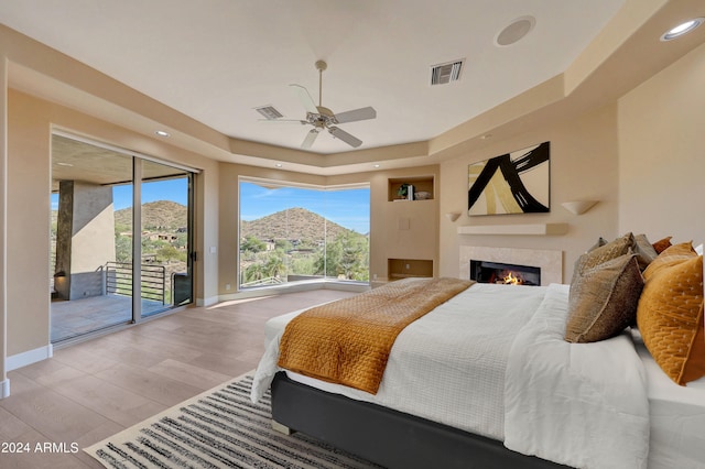 bedroom featuring access to exterior, ceiling fan, a tray ceiling, a mountain view, and light wood-type flooring