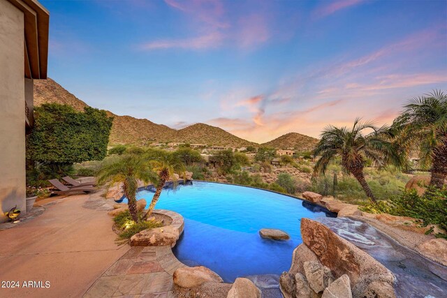 pool at dusk featuring a mountain view and a patio area