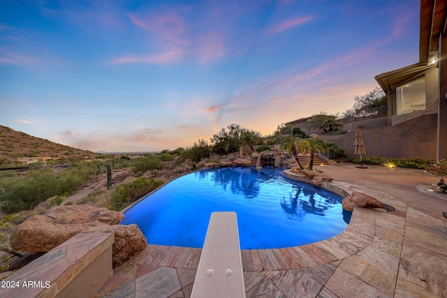 pool at dusk with a diving board and a patio