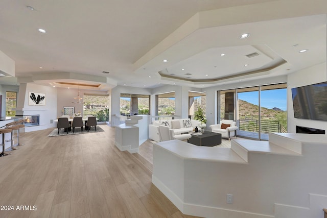 living room with a fireplace, a raised ceiling, and light wood-type flooring