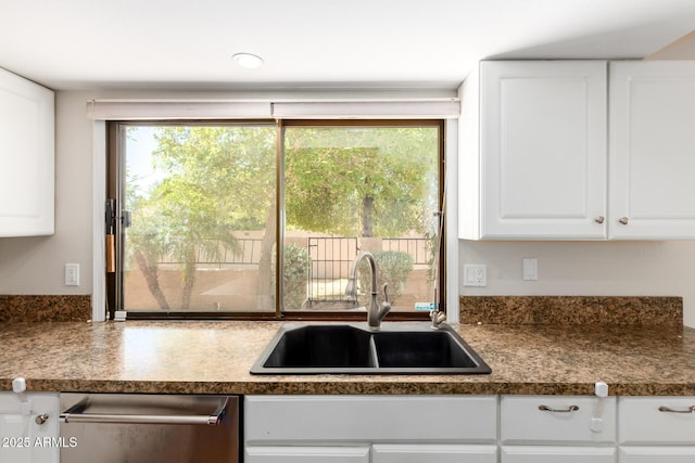 kitchen featuring stainless steel dishwasher, a sink, white cabinets, and dark countertops