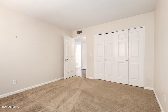 unfurnished bedroom featuring baseboards, light colored carpet, visible vents, and a closet