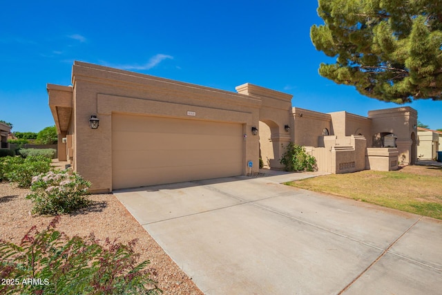 pueblo-style home with an attached garage, stucco siding, and driveway