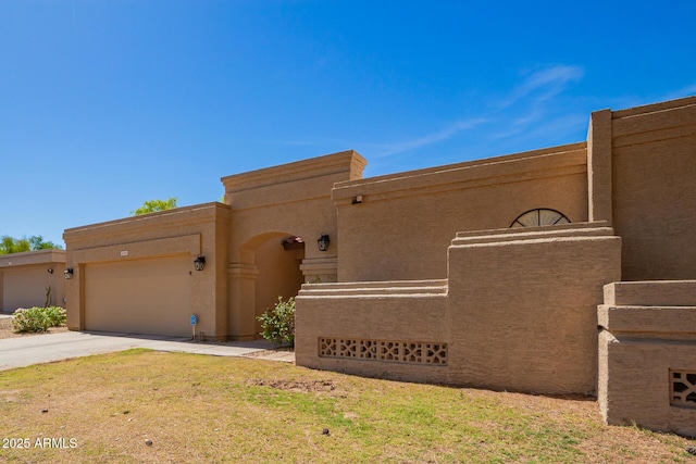 pueblo-style house with a front lawn, an attached garage, concrete driveway, and stucco siding