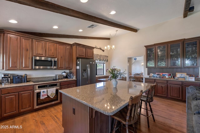kitchen with appliances with stainless steel finishes, a kitchen breakfast bar, light wood finished floors, light stone countertops, and recessed lighting