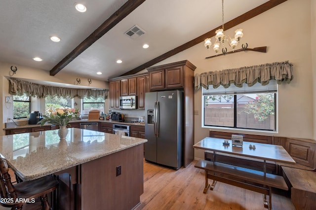 kitchen featuring appliances with stainless steel finishes, light stone counters, a chandelier, light wood-style flooring, and a kitchen island