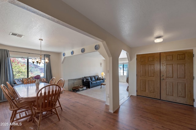 dining room featuring wood finished floors, a chandelier, a textured ceiling, and arched walkways
