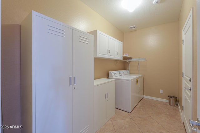 washroom featuring washing machine and dryer, cabinets, a textured ceiling, and light tile patterned flooring