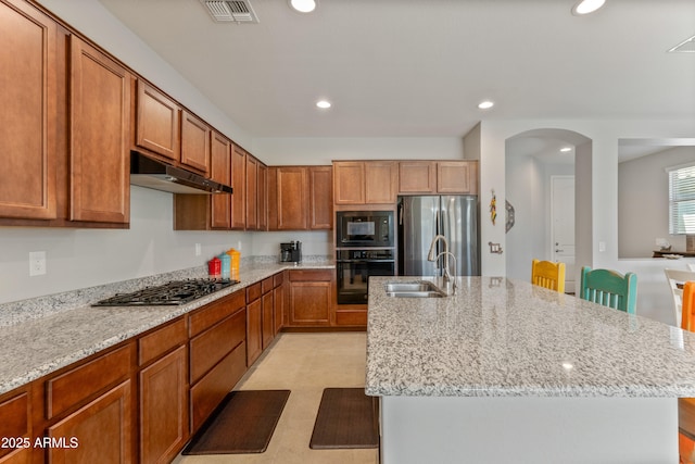 kitchen featuring sink, a breakfast bar area, an island with sink, light stone countertops, and black appliances