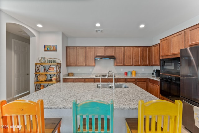 kitchen featuring light stone countertops, sink, a breakfast bar area, and black appliances