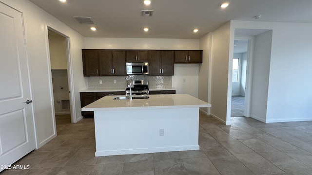 kitchen featuring tasteful backsplash, appliances with stainless steel finishes, sink, and a center island with sink