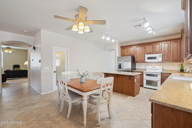 kitchen featuring visible vents, light tile patterned floors, arched walkways, white appliances, and a sink