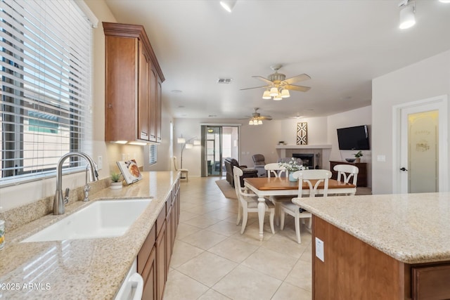 kitchen with brown cabinets, a tiled fireplace, a sink, open floor plan, and light tile patterned floors