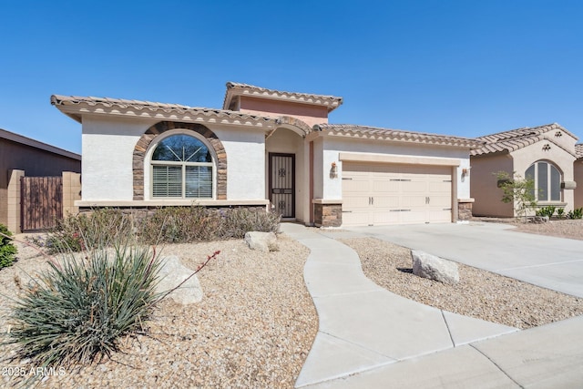 mediterranean / spanish house with stucco siding, a tile roof, stone siding, concrete driveway, and an attached garage