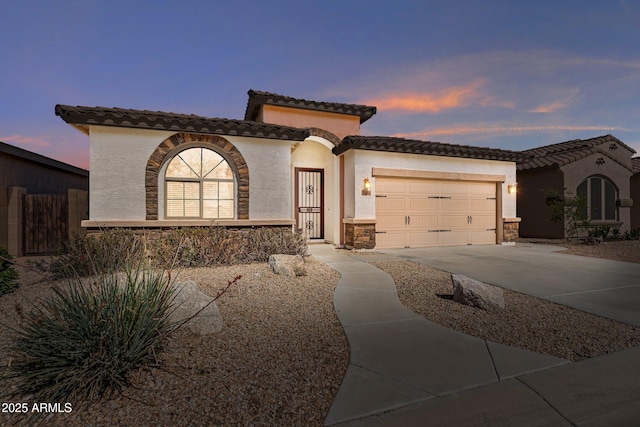 mediterranean / spanish house with a tiled roof, stucco siding, driveway, stone siding, and an attached garage