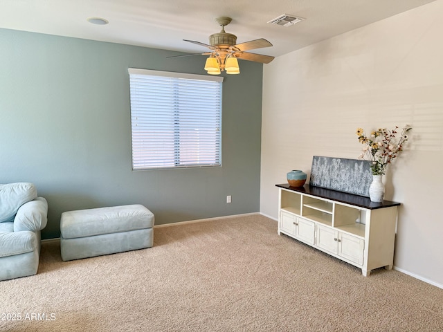 living area with visible vents, baseboards, light colored carpet, and ceiling fan