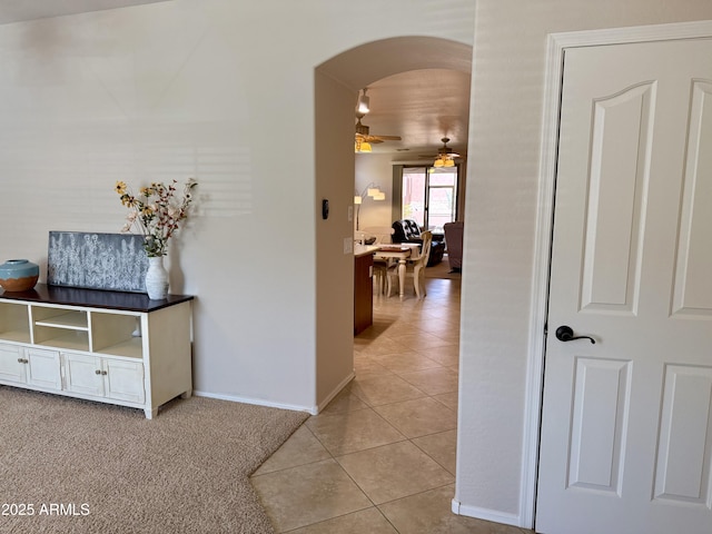 hallway featuring light colored carpet, light tile patterned floors, baseboards, and arched walkways