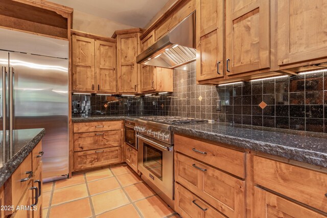 kitchen featuring tasteful backsplash, high quality appliances, brown cabinets, light tile patterned flooring, and exhaust hood