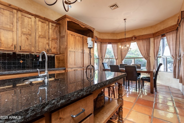 kitchen featuring decorative backsplash, brown cabinetry, visible vents, and an inviting chandelier