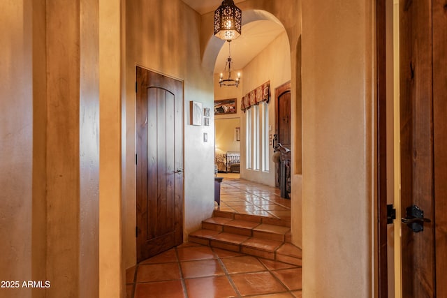 hall with arched walkways, a chandelier, and tile patterned floors