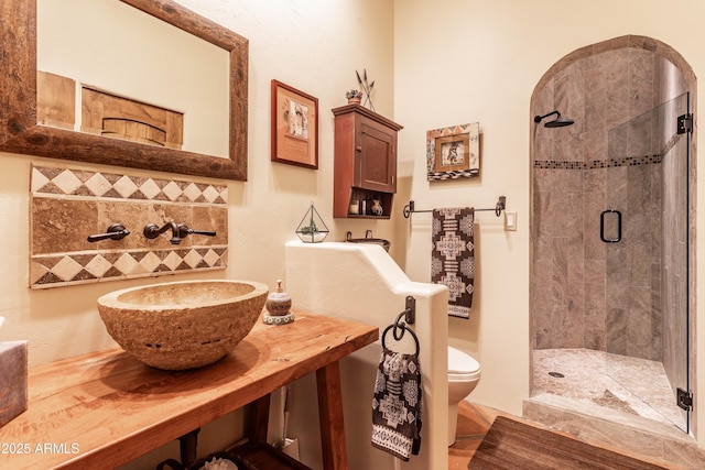 full bathroom with decorative backsplash, toilet, a sink, and a stall shower