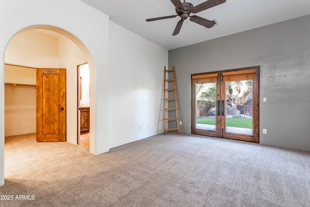 carpeted spare room featuring ceiling fan and arched walkways