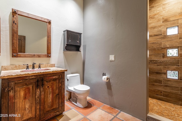 bathroom featuring tiled shower, toilet, tile patterned flooring, a textured wall, and vanity