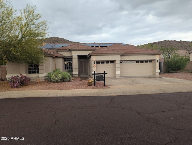 view of front of home featuring a garage, driveway, roof mounted solar panels, stucco siding, and a tiled roof