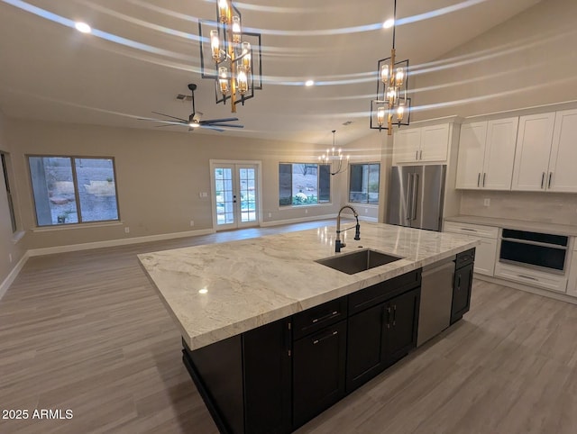 kitchen featuring appliances with stainless steel finishes, a chandelier, a sink, light wood-style flooring, and dark cabinetry