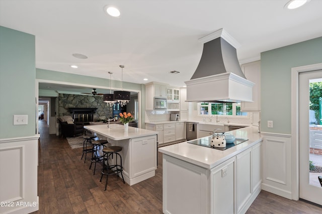 kitchen with premium range hood, appliances with stainless steel finishes, a kitchen island, white cabinetry, and a kitchen breakfast bar