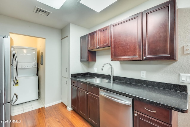 kitchen with visible vents, appliances with stainless steel finishes, light wood-style floors, stacked washer / drying machine, and a sink